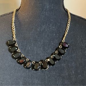 Black statement necklace with gold tone chain.